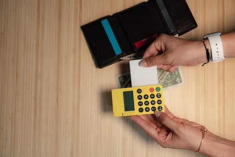 Person making payment with empty wallet and yellow card reader on wooden surface