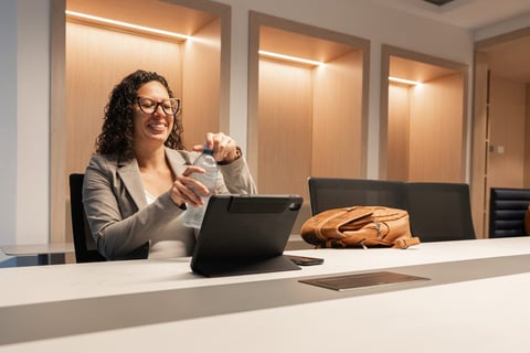 Woman with curly hair and glasses working on laptop at modern office desk with pastry and coffee